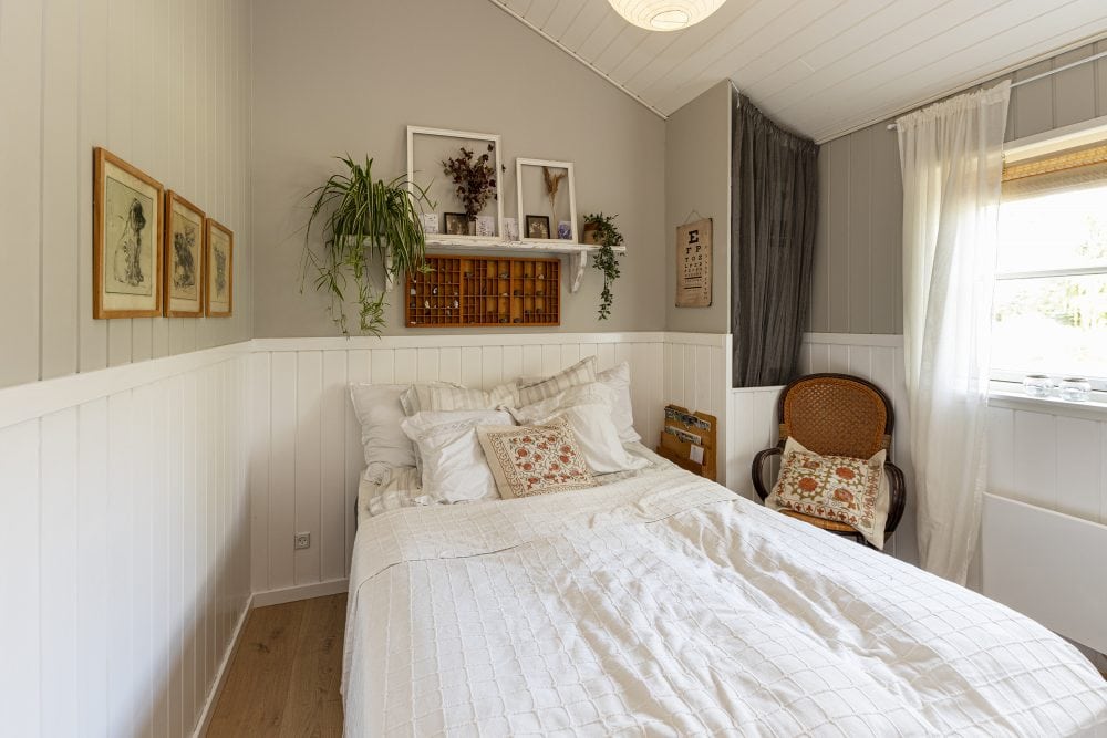 Hyggeligt soveværelse med træbeklædte vægge, dobbeltseng, stol, billeder og vindue