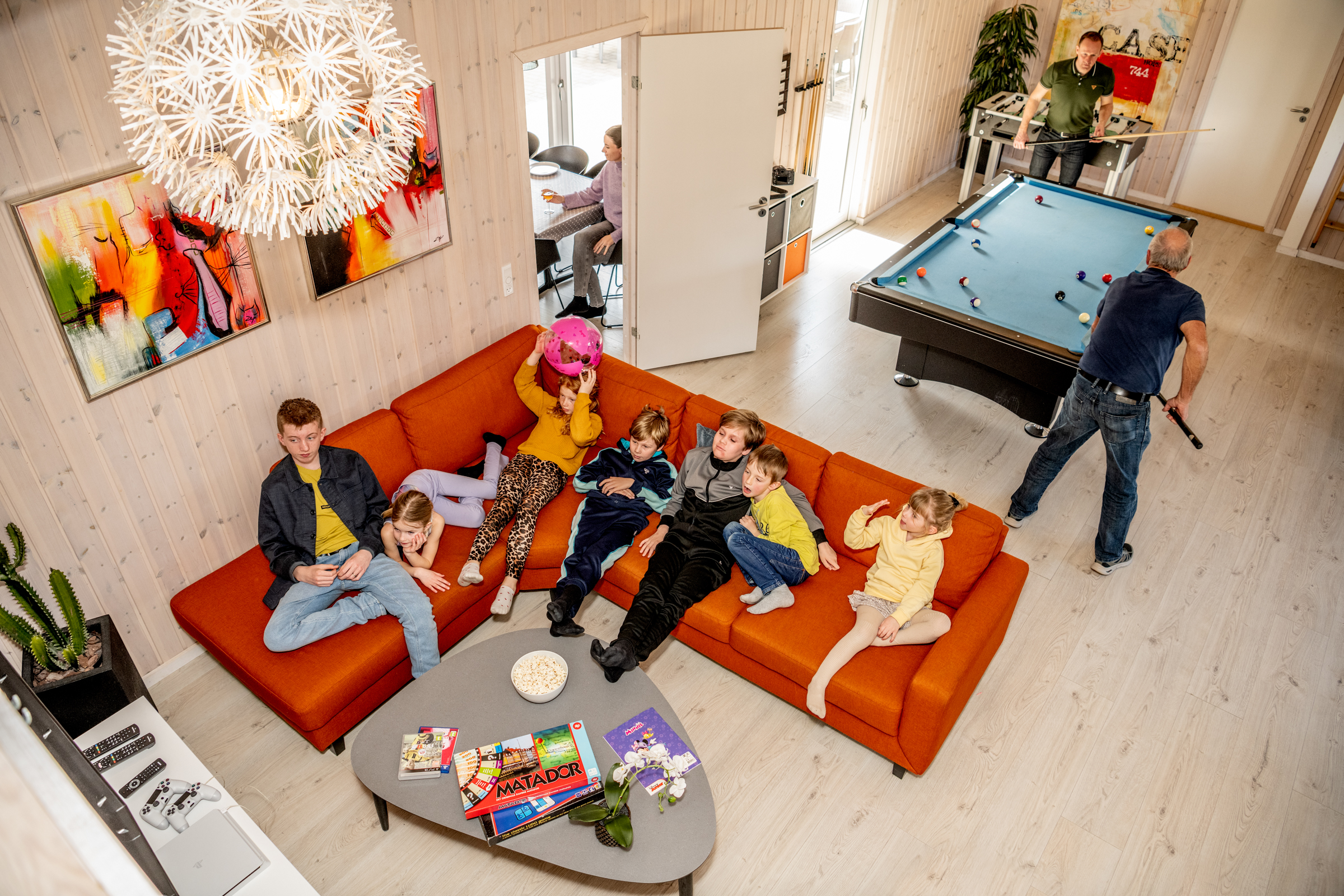 Aktivitetsrum i sommerhus med børn der ser tv og mænd der spiller billard